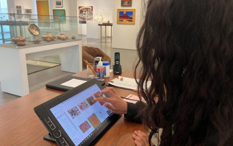 Young woman sitting in an art gallery with a tablet showing images of artworks 